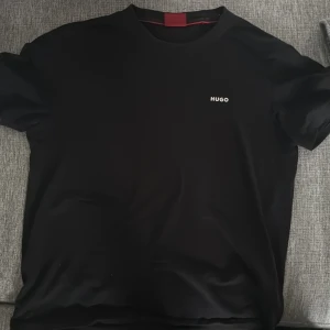 Svart t-shirt från Hugo Boss - Snygg svart t-shirt från Hugo Boss med diskret vit HUGO-logga på bröstet. Klassisk rund halsringning och korta ärmar. Perfekt för en clean och stilren look.
