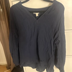 Mörkblå blus från H&M med v-ringning - Säljer en mörkblå blus från H&M i storlek S. Blusen har v-ringning, långärmade ärmar och är tillverkad i ett lätt, krinklat tyg som ger en avslappnad vibe. Perfekt för dig som gillar en enkel men snygg look.