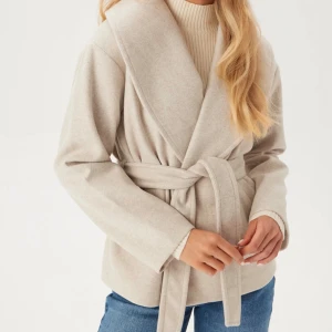 Beige omlottjacka med bälte - Snygg beige omlottjacka med bred krage och knytbälte i midjan. Jackan har en stilren och enkel design med lång ärm. Helt ny använd 1 gång😍 har självklart egna bilder bara säga till så skickar jag😊