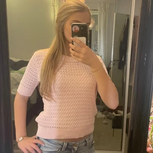 Ljusrosa stickad topp från 157 - Säljer en ljusrosa stickad topp från 157 med korta ärmar och rund hals. Storlek M men passar som S. Toppen har ett snyggt hålmönster och ribbade muddar vid ärmslut och nederkant. Perfekt för vår och sommar när du vill ha en söt och luftig look.🐝🥰