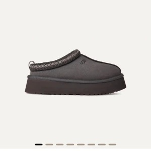 UGG slip-on med plattform - Säljer ett par mörkgråbruna slip-on skor från UGG med plattformsula och rund tå. Ovandelen är i mjuk mocka och insidan är fodrad med fluffigt material för extra komfort. Dekorativt mönster runt öppningen och praktisk hälflik. Perfekt för säsongen. Testade en gång, kommer i kartongen som skorna kom i som nya! Säljer då jag valde fel på storleken. 