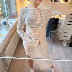 Vit stickad långklänning med öppen rygg ifrån Na-Kd - Supersnygg vit stickad långklänning med rund hals och långa ärmar. Klänningen har ett coolt strukturerat mönster och en öppen rygg som ger en extra touch. Passformen är slim och materialet är mjukt och stretchigt, perfekt för dig som gillar att sticka ut. Jag har använt den som strandklänning över en bikini, men funkar till mycket mer! Klänningen har en liten fläck på övre låret, men ingenting som syns när man har den på 🤍