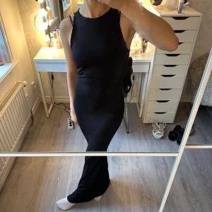 Svart långklänning med ärmlös design från Ginatricot - Supersnygg svart långklänning med ärmlös och figurnära passform. Klänningen har en rund halsringning och slät yta utan mönster eller detaljer. Perfekt för dig som gillar minimalistisk och stilren look. Aldrig använd 🖤