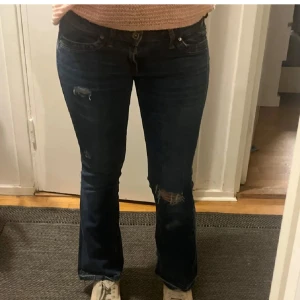 Mörkblå bootcut jeans med slitningar - Snygga mörkblå jeans med bootcut-modell och slitna detaljer på låret och knät. Jeansen har klassisk femficksdesign och låg midja. Perfekta för dig som gillar en avslappnad och trendig stil.