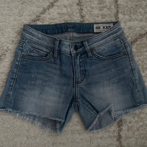 Blå jeansshorts från Crocker  - Snygga blå jeansshorts från Crocker i storlek XXS. Klassisk femficksmodell med råa, fransiga benslut och slitna detaljer. Shortsen har normal passform och är perfekta för sommaren. Tillverkade i bomull för en skön känsla.
