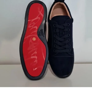 Christian marinblå mockasneakers - Snygga marinblå sneakers från Christian  i mjuk mocka med klassisk röd sula och broderad logga baktill. Skorna har rund tå, platt sula och snörning. Perfekta för dig som vill ha en lyxig och stilren look med en ikonisk touch.