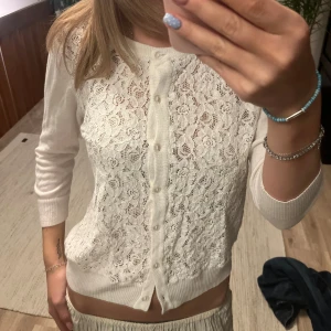 Vit spetskofta från Lindex - Superfin vit kofta från Lindex med spets framtill och knappar hela vägen. Långärmad och i mjukt material, perfekt för lager-på-lager. Snygg ribbad kant nedtill och vid ärmslut. Passar dig som gillar romantiska detaljer och stilren look.