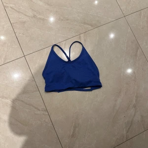 Blå linnetopp från Relode - Säljer en blå linnetopp från Röhnisch med smala axelband som korsas i ryggen. Toppen har en sportig look och är tillverkad i mjukt bomullsmaterial. Perfekt för träning eller chill dagar. Diskret logga i vitt på sidan. Snygg och enkel design!