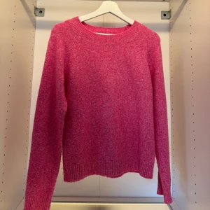 Rosa stickad tröja med rund hals - Mysig rosa stickad tröja med rund halsringning och ribbade muddar vid ärmslut och nederkant. Perfekt för dig som vill ha en enkel men färgstark tröja till garderoben. Långärmad och i en skön, mjuk kvalitet.