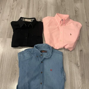 Tre skjortor från Burberry, Ralph Lauren & Morris - Säljer tre skjortor: en svart Burberry med klassiskt rutigt mönster i kragen, en ljusrosa Ralph Lauren med broderad logga och en ljusblå jeansskjorta från Morris Stockholm. Och jag vill ha bud.