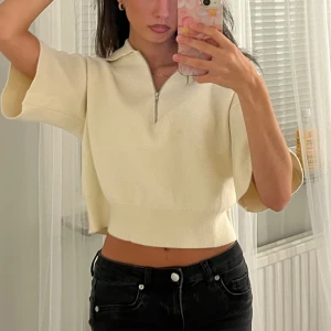 Ljusbeige croppad tröja - Säljer en ljusbeige croppad tröja med half zip och krage. Tröjan har korta, vida ärmar och en avslappnad passform. 