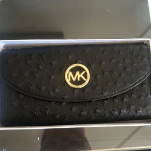 Svart plånbok Michael Kors skinn - Snygg svart plånbok från Michael Kors i präglat skinn med guldfärgat MK-emblem framtill. Plånboken har flera fack, dragkedja inuti och tryckknappsstängning. Perfekt storlek för att ha med sig överallt till sin outfit! Fick den i julklapp för några jular sedan! Perfekt julklapp nu mot hösten till sin syster eller Mamma exempelvis 💗🤌