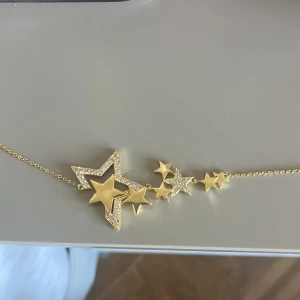 Guldigt stjärnhalsband från Ioaku - Supersnyggt halsband från Ioaku i guld med flera stjärnor i olika storlekar. Några av stjärnorna är dekorerade med glittriga stenar som ger extra bling. Perfekt statement-piece för dig som gillar unika smycken med cool design. skrih privat för frågor! aldrig använt