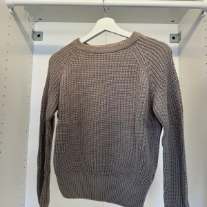 Beige stickad tröja med grov struktur - Säljer en beige stickad tröja med grov struktur och rund halsringning. Tröjan har långa ärmar och breda ribbade muddar vid ärmslut och nederkant. Perfekt för lager-på-lager under kyliga dagar.