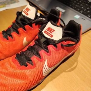 Nike Zoom Rival M löparskor röd/vit - Nike Zoom Rival M är grymma löparskor med spik för banlöpning. Använda 1 gång(på bana) så i princip nyskick. Inga anmärkningar alla. Skorna är röda med svarta och vita detaljer, har svart snörning och en vit Nike-logga på sidan. Ovandelen är i syntetmaterial och sulan har flera spikar för max grepp på banan.