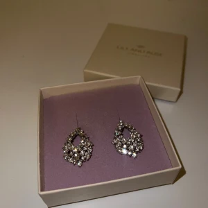 Glittriga örhängen från Lily and Rose - Säljer ett par snygga örhängen från Lily and Rose i silverfärg med massor av glittrande stenar. De har en droppformad design och är riktigt statement med sitt gnistrande utseende. Perfekta om du vill sticka ut och addera lite extra bling till din look.