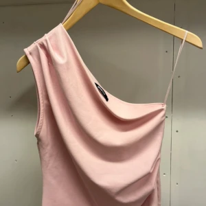 Ljusrosa oneshoulder topp Gina Tricot - Supersnygg ljusrosa topp från Gina Tricot med trendig oneshoulder-design och tunn axelrem. Mjuk och följsam i materialet, perfekt för dig som vill sticka ut med en enkel men cool look.