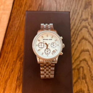 Michael Kors Ritz klocka - Stilren klocka från Michael Kors i silverfärgat rostfritt stål med länkarmband. Urtavlan är i pärlemor med glittriga stenar som markeringar, tre mindre urtavlor och datumvisning. Batteriet behöver bytas.