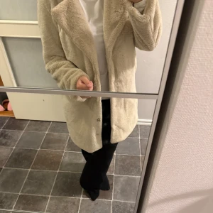 Beige fuskpälsjacka från NAKD - Mysig beige pälsjacka från NAKD med klassisk krage och knäppning framtill. Jackan är fodrad och har en rak, lite längre modell som ger en chill och trendig vibe. Perfekt för kalla dagar när du vill vara både varm och snygg. Mittersta knappen på jackan saknas, men de är inget som syns när den är knäppt/ öppen. Sen har även ett litet hål i armen innifrån, vilket inte heller syns när man har på sig den🤍
