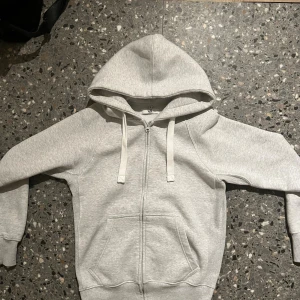 Ljusgrå hoodie från Russemerch  - Ljusgrå hoodie från R i storlek M. Klassisk modell med huva, dragsnören och hel dragkedja framtill. Mjuk insida och två stora fickor framtill. Perfekt för chill dagar eller när du vill ha en enkel och stilren look.