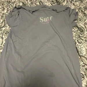 Oversized grå t-shirt Jack & Jones - Snygg oversized t-shirt från Jack & Jones i en dov grå färg. Tryck på ryggen med palmblad och texten 'Palm Luna', samt mindre tryck framtill med 'Surf City'. Tillverkad i mjuk bomull, perfekt för en chill look. Finns en fläck syns på första bilden