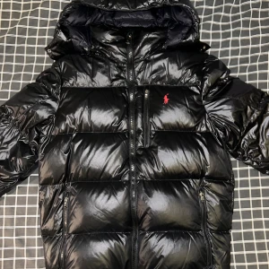 Svart pufferjacka från Polo Ralph Lauren - Perfekt till vintern! Svart, glansig pufferjacka från Polo Ralph Lauren med luva. Storlek L, Ordinarie pris 6 499:- För stor för mig så är intresserad av byte till M eller S, jag är 176.
