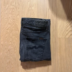  Nudie Jeans lean Dean färg grey fog - Snygga svarta skinny jeans från Nudie Jeans med klassiska bakfickor och diskret logga. Jeansen har smal passform och är tillverkade i mjukt denimtyg som sitter tajt längs benen. Perfekta för dig som gillar en stilren och modern look.