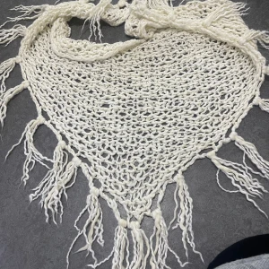 Vit stickad trekantig halsduk med fransar - Säljer en vit, grovstickad trekantig halsduk med långa fransar längs kanterna. Halsduken har en luftig och bohemisk känsla, perfekt att slänga över axlarna för en chill look. Mjuk och skön, passar dig som gillar unika accessoarer.