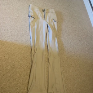 Beiga cargopants med bootcut - Snygga beiga cargopants med bootcut-snitt och praktiska fickor på sidorna. Byxorna har en klassisk midja och stängs med dragkedja och knapp framtill. Perfekta för dig som gillar en avslappnad men trendig stil.