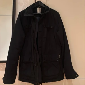Fieldjacket J.lindberg stl L/M - Svart Fieldjacket från J.Lindberg i storlek L/M passar 185 cm, 79 kg. Inga defekter men har tecken på användning. Fråga eller lägg prisförslag!