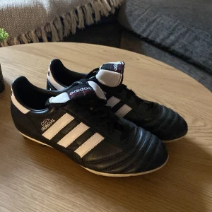 Adidas Copa Mundial fotbollsskor svart/vit - Klassiska Adidas Copa Mundial fotbollsskor i svart och vitt med de ikoniska tre ränderna på sidan. Skorna har snörning, rund tå och platt sula med fasta dobbar för gräsplan. Tillverkade i mjukt skinn för bästa komfort och känsla på planen. Nypriss ca 1300kr
