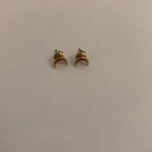 Guldiga örhängen med månmotiv - Säljer ett par små örhängen i form av halvmånar i guldig färg. De är stilrena och har en enkel men cool design som passar perfekt om du gillar detaljer med lite mystisk vibe. Perfekta att mixa med andra smycken för en personlig look. Riktig guld!