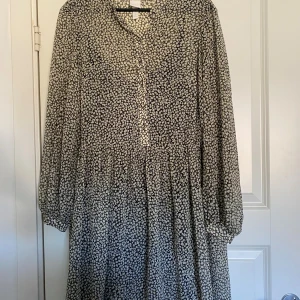 Blommig klänning - Klänning med svart botten och små  blommor, v-ringad med knappar framtill och långa ärmar med lätt puff. 