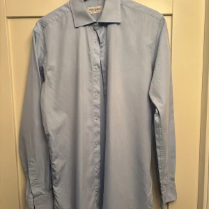 Ljusblå skjorta från John Henric - Snygg ljusblå skjorta från John Henric med klassisk krage och knappar framtill. Skjortan är långärmad och har en stilren, enkel design som passar till många olika looks. Tillverkad i mjuk bomull för skön känsla hela dagen.