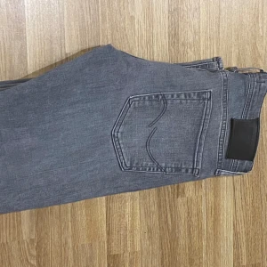 Grå jeansbyxor i storlek 30/32 - Säljer ett par grå jeansbyxor i klassisk femficksmodell. Byxorna har raka ben och normal passform, tillverkade i mjukt jeanstyg. Perfekta för dig som gillar en stilren och enkel look. Storlek 30/32.