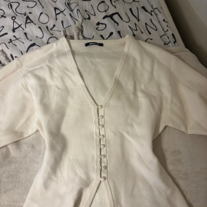 Beige kofta från Gina Tricot - Superfin beige kofta med v-ringning och dekorativa knappar framtill. Långärmad och figurnära passform, perfekt att styla med smycken. Mjuk och skön, passar både till jeans och kjol.