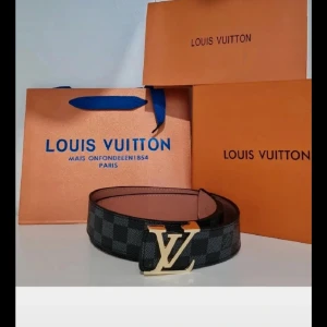 L&V rutigt skärp i skinn - Snyggt L&V bälte i svart och grått rutigt mönster med ikoniskt L&V-spänne i guld. Bältet är tillverkat i skinn och har en exklusiv känsla, perfekt för att lyfta vilken outfit som helst. Kommer med originalförpackning och dustbag.