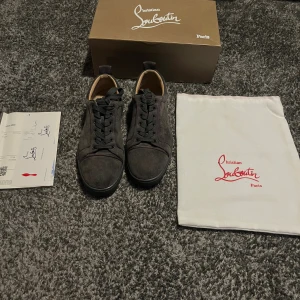Gråa Christian Louboutin skor - Snygga gråa sneakers från Christian Louboutin i mocka med röd sula. Allt som är med på bilden följer med. Använda men i bra skick. Perfekta för dig som vill ha en lyxig och stilren look. Skriv för mer info. 