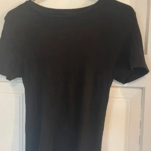 Svart ribbad topp från FSBN Sister - Svart ribbad topp från FSBN Sister i storlek S. Modellen har rund hals och korta ärmar, perfekt för en enkel och clean look. Materialet är mjukt och stretchigt, vilket gör den skön att bära. Snygg att matcha med jeans eller kjol.