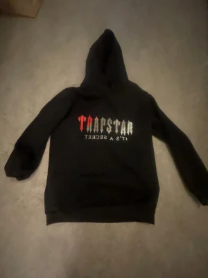 Svart Hoodie från märket Trapstar - Svart Trapstar hoodie. Den här hoodien håller dig varm nu eftersom det är vinter och är i mycket bra skick. Jag säljer den här i hoodien i storleken XXS. Barn som är från åldern 10-12 år kommer förmodligen kunna ha på sig denna hoodien.