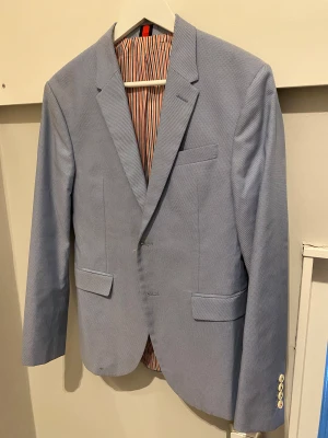 Ljusblå kavaj från Zara Man - Snygg ljusblå kavaj från Zara Man med klassisk passform och två fickor framtill. Insidan har ett coolt randigt foder i orange, blått och vitt. Perfekt för dig som vill ha en stilren look till sommarens fester. Kavajen har knappar vid ärmslut och diskreta detaljer. (Pris kan diskuteras vid smidig affär)