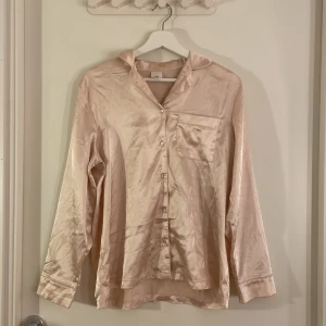 Ljusrosa silkesliknande pyjamas skjorta från gekås Ullared  - Snygg ljusrosa pyjamas skjorta i silkesliknande material från gekås Ullared . Skjortan har klassisk krage, bröstficka och knappar framtill. Långärmad och med en mjuk, glansig finish som ger en lyxig känsla. Små fläckar på rygg och arm!