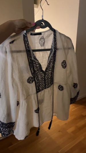 Blus från ZARA - Säljer en super söt vit blus från ZARA med mörkblå broderade detaljer och mönster över hela toppen. Helt oanvänd, köpt i Spanien. 