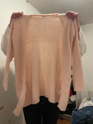 Ljusrosa kofta från KappAhl - Mysig ljusrosa kofta från KappAhl med öppen front och två praktiska fickor framtill. Koftan är stickad och har långa ärmar, perfekt för lager-på-lager-stil. Enkel och stilren design som passar till allt.