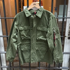 Grön Fieldjacka - Snygg militärgrön fieldjacka från Alpha Industries med flera stora fickor, klassisk krage från deras provkollektion. Jackan är i bomull och har tryckknappar med innerfickor. Nypris 1800. Kom gärna med frågor och funderingar!!