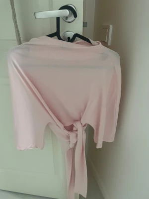 Ljusrosa omlottopp från Gina Tricot - Supersöt ljusrosa omlottopp från Gina Tricot med knyt bakom. Tunn och luftig med trekvartsärmar, perfekt för vår och sommar. Enkel att styla till både jeans och kjol för en fräsch look.