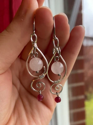 Handgjorda örhängen med rosenkvarts - Unika örhängen i silvrig metalltråd med snirklig design, dekorerade med ljusrosa rosenkvarts och små mörkröda pärlor. Perfekt statement-accessoar för dig som gillar boho och ädelstenar.