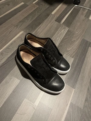 Lanvin skor Byte inte sälja - Svarta sneakers med vit platt sula och rund tå. Ovandelen är i en mix av skinn och mocka, utan snören men med metallhål för snörning. Snygg och enkel design som passar till det mesta. Byter!