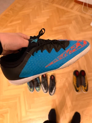 Nike futsal skor  - Säljer ett par grymma Nike fotbollsskor i blått och svart med coola orange detaljer och mönstrad sula. Skorna har snörning och platt sula, perfekt för inomhusspel. Materialet är syntet och designen är riktigt sportig med en snygg grafisk touch på sidan.