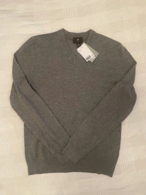 Grå v-ringad tröja från H&M Slim Fit - Grå v-ringad tröja från H&M i slim fit-modell. Tillverkad av 65% LivaEco viskos, vilket gör den mjuk och skön. Tröjan har långa ärmar och ribbade muddar vid hals, ärmslut och nederkant. Perfekt för dig som gillar stilrena och enkla plagg. Hör av dig vid eventuella frågor!! 😀🙌